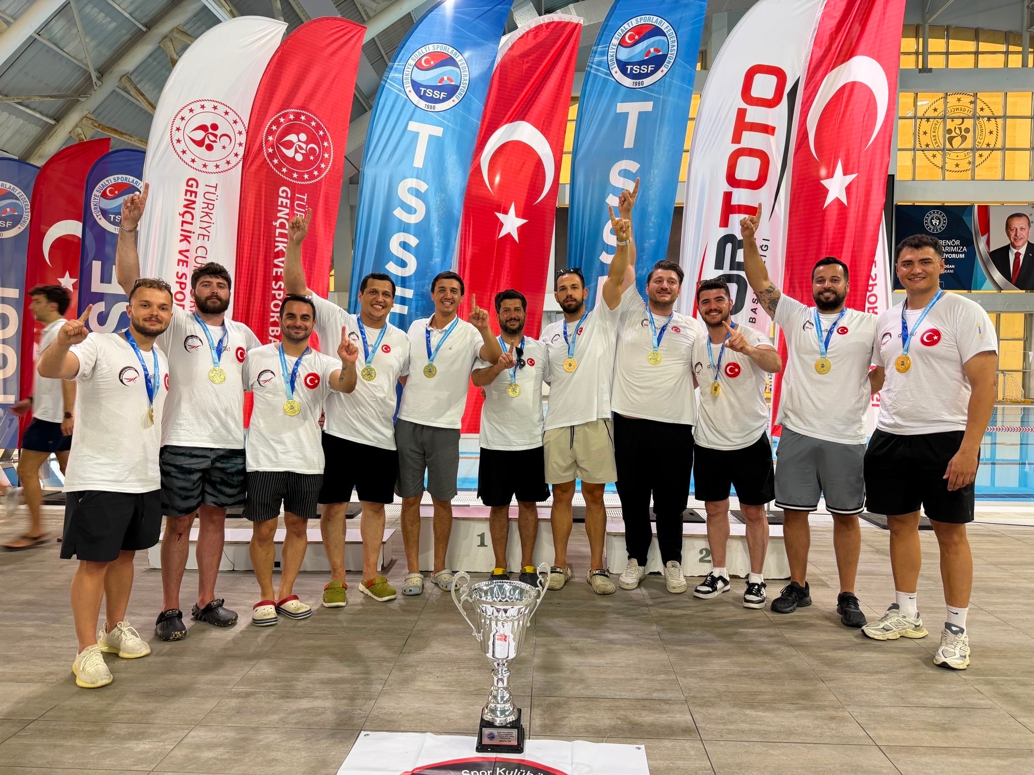 Federasyon bayrakları önünde kupa ve madalyalarla şampiyonluğu kutlayan erkek sualtı hokeyi takımı